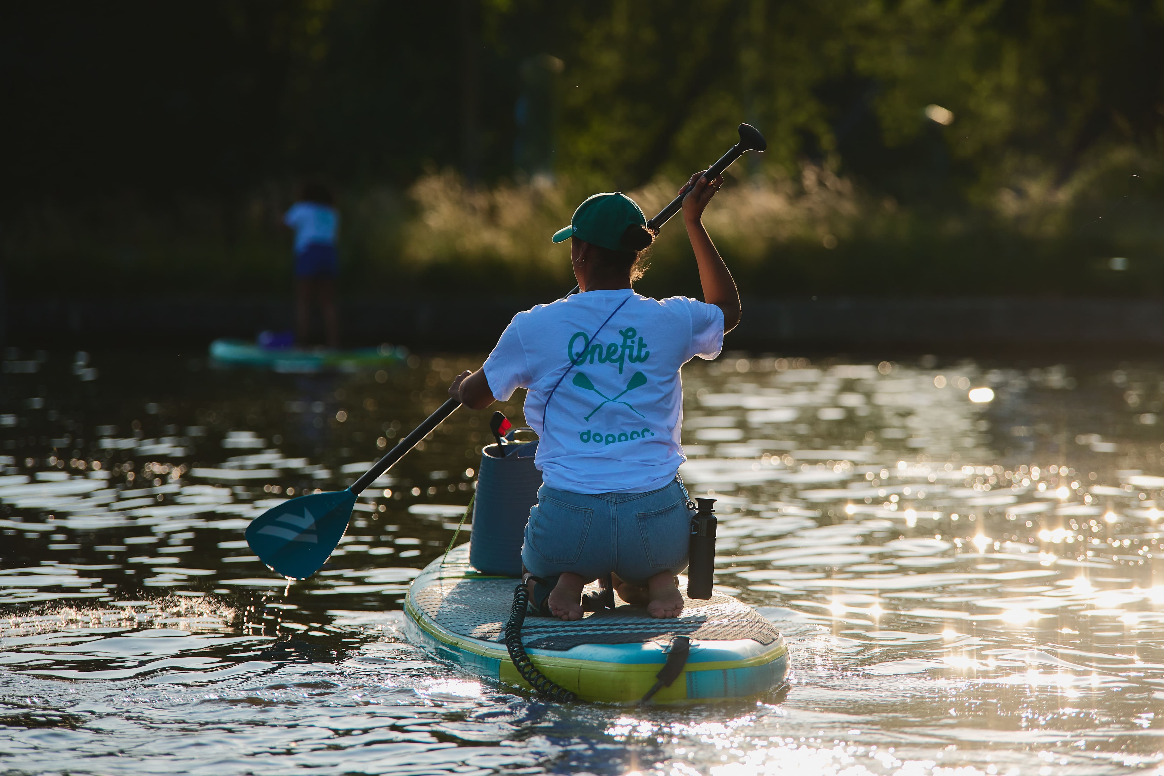 Woman on sup board paddling with a black Dopper bottle