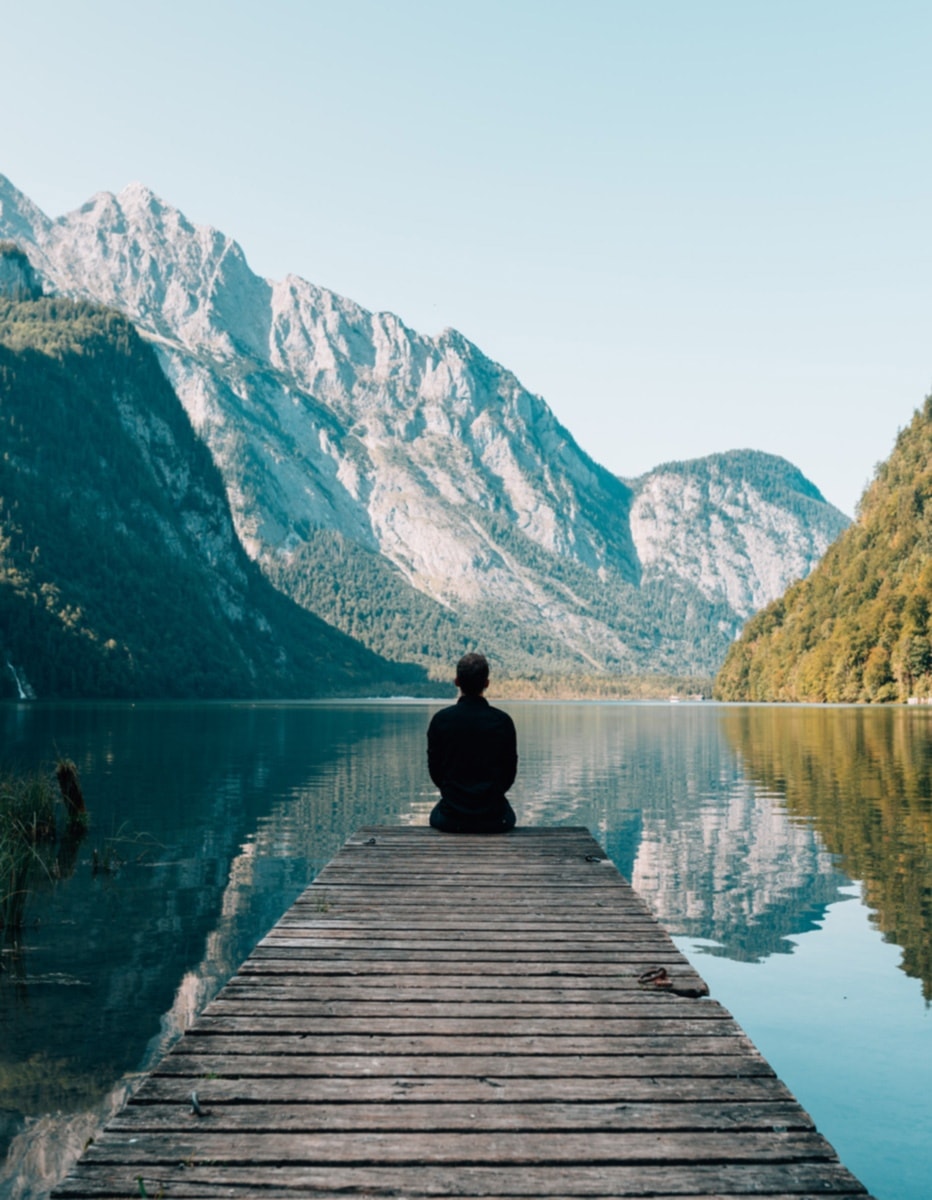 Person sitting on the end of a pier with a view on the lake and mountains